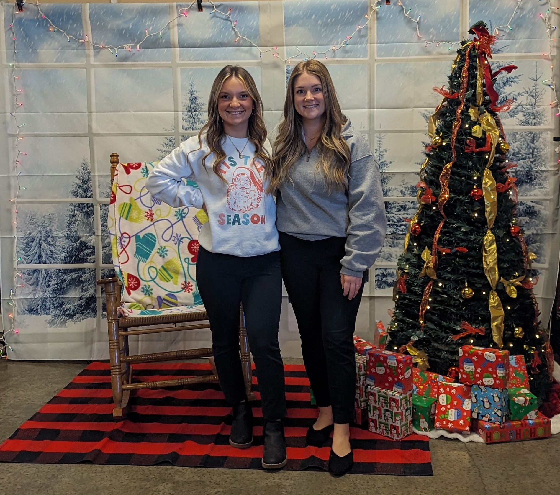 Kasey Johnston and Holly Wolfe pose in front of a Christmas backdrop and tree.